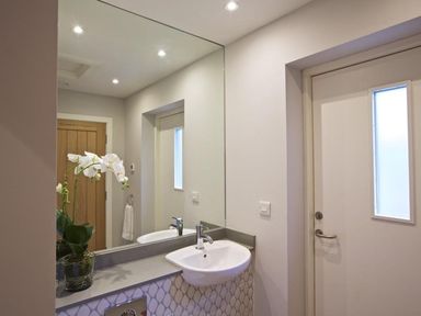 A bathroom with a white sink and faucet a large mirror a potted orchid a wooden door and a white door with a window at 3 The Drive Hillfield Village Dartmouth