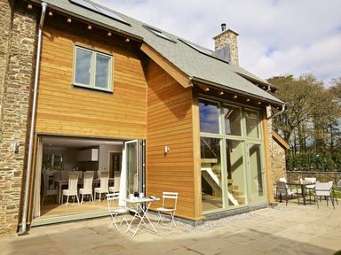 A wooden house exterior with large windows and open doors leading to an interior dining area with chairs and tables at 3 The Drive Hillfield Village Dartmouth