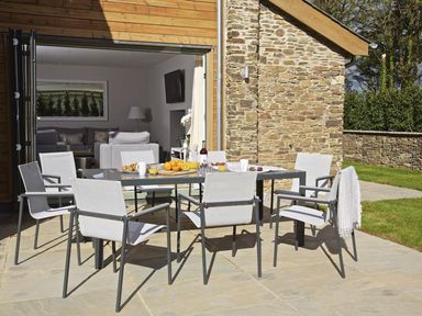 An outdoor patio with a dining table and six chairs set with food and drinks outside a house with stone and wood exterior at 3 The Drive Hillfield Village Dartmouth
