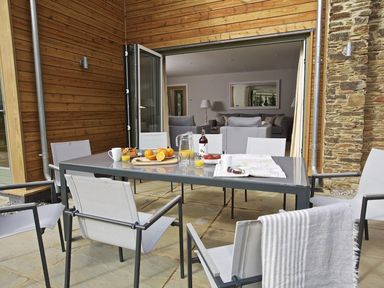An outdoor dining area with a table set with breakfast items and chairs on a stone patio at 3 The Drive Hillfield Village Dartmouth