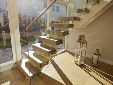 A modern floating staircase with wooden steps and glass railing next to two metal lanterns at 3 The Drive Hillfield Village in Dartmouth