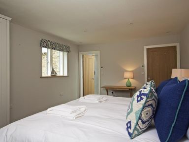 A bedroom with a bed with pillows and towels a wooden door a table with a lamp and a window at 3 The Drive Hillfield Village Dartmouth