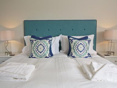 A bedroom with a bed with blue and white patterned pillows white bed linens and bedside tables with lamps at 3 The Drive Hillfield Village in Dartmouth