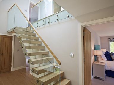A staircase with wooden steps and glass railings next to a bedroom with a bedside table and lamp at 3 The Drive Hillfield Village in Dartmouth