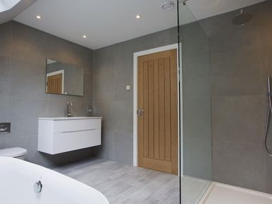 A bathroom with a bathtub sink mirror wooden door and glass shower at 3 The Drive Hillfield Village Dartmouth