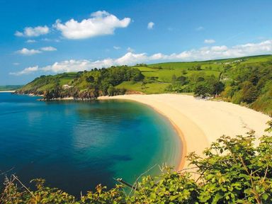 A beach with clear water next to green hills and trees at 3 The Drive Hillfield Village in Dartmouth