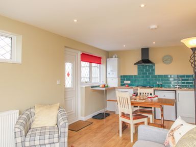 A kitchen and dining area with a table set for tea and a checkered armchair at Roundham Cottage in West Bay