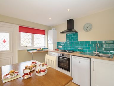 A kitchen with a dining table set with tea cups and muffins and green tiled backsplash at Roundham Cottage in West Bay