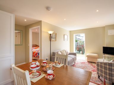 A living room with a dining table set with cups and pastries a sofa armchair and TV at Roundham Cottage in West Bay
