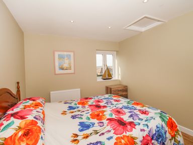 A bedroom with a floral bedspread a wooden bedside table a small window with a model sailboat and a framed picture on the wall at Roundham Cottage in West Bay