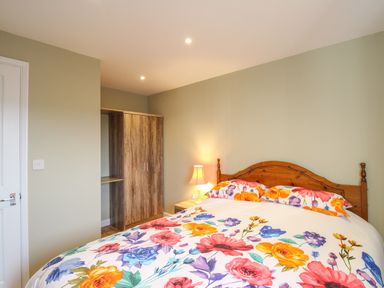 A bedroom with a wooden bed frame floral bedding a wooden wardrobe a bedside table and lamp at Roundham Cottage in West Bay