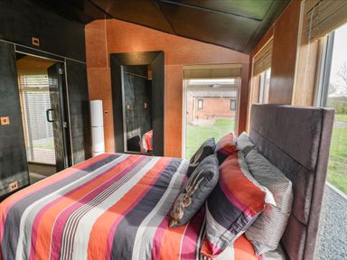 A bedroom with a bed and striped bedding near large windows showing a grassy yard at The Tractor Shed in Lower Broadheath Worcester