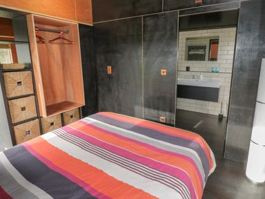 A bedroom with a striped bedspread wooden wardrobe with hangers and an open doorway leading to a bathroom at The Tractor Shed in Lower Broadheath Worcester