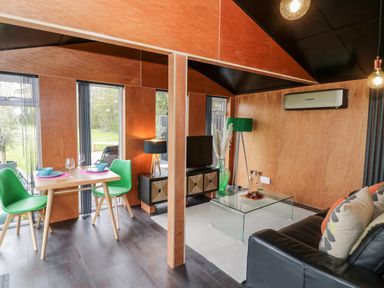 A living area with green chairs a wooden table and a sofa with cushions at The Tractor Shed in Lower Broadheath Worcester