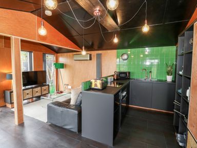 A kitchen and living area with green tiled backsplash and a black sofa at The Tractor Shed in Lower Broadheath Worcester