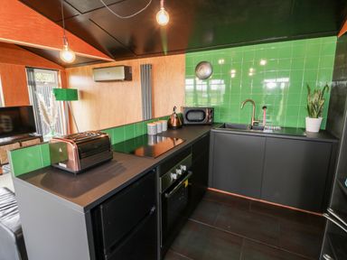 A kitchen with green tiled backsplash black cabinets and countertop appliances at The Tractor Shed in Lower Broadheath Worcester