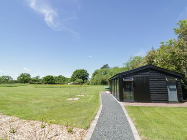A black wooden building next to a gravel pathway in a grassy field at The Tractor Shed in Lower Broadheath Worcester