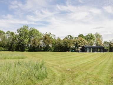 A large grassy field with a small black building and trees in the background at The Tractor Shed in Lower Broadheath Worcester
