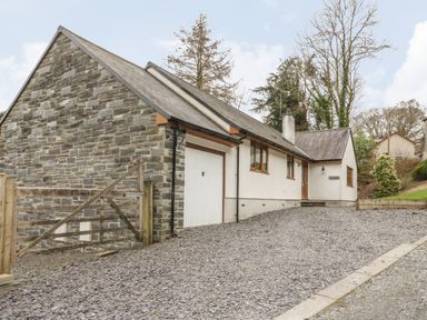 A house with a stone wall garage and a gravel driveway at Bryn Elsi in Betws Y Coed