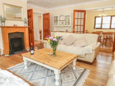 A living room with a wooden coffee table holding a vase of flowers and a bottle of wine and two glasses near a fireplace and sofas at Bryn Elsi in Betws-Y-Coed