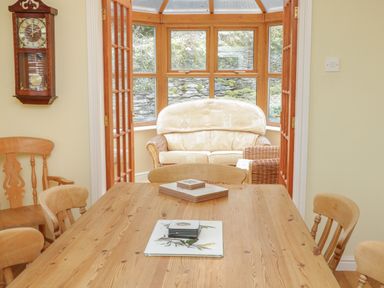 A dining room with a wooden table and chairs opening to a sunroom with a cushioned sofa at Bryn Elsi in Betws-Y-Coed