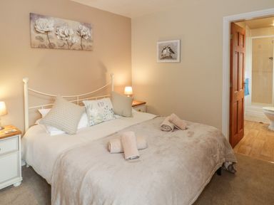 A bedroom with a double bed with pillows and rolled towels bedside tables with lamps and an open door to an ensuite bathroom at Bryn Elsi in Betws-Y-Coed