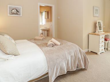 A bedroom with a bed, pillows, rolled towels, a dressing table with a mirror and stool, and an adjoining bathroom at Bryn Elsi in Betws-Y-Coed