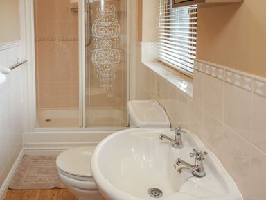 A bathroom with a sink, toilet, shower with glass doors, and a window with blinds at Bryn Elsi in Betws-Y-Coed