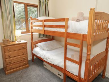 A bedroom with wooden bunk beds and a wooden chest of drawers with a lamp near a window at Bryn Elsi in Betws-Y-Coed