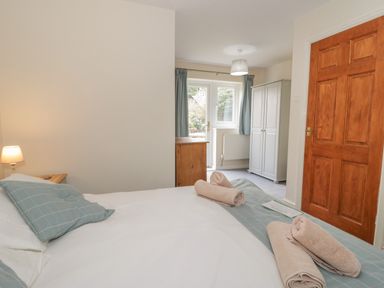 A bedroom with a bed pillows towels bedside lamp wooden door wardrobe and window with curtains at Bryn Elsi in Betws-Y-Coed