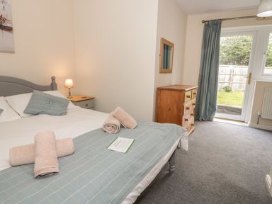 A bedroom with a bed, bedside table with lamp, chest of drawers, and a door leading to a garden at Bryn Elsi in Betws-Y-Coed