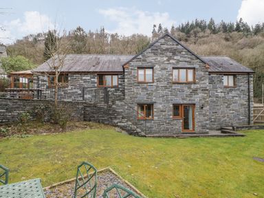 A stone house with multiple windows and a garden with metal chairs and table at Bryn Elsi in Betws-Y-Coed