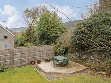 An outdoor wooden deck with a metal table and chairs next to a stone wall and wooden fence at Bryn Elsi in Betws-Y-Coed