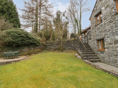 A grassy garden with stone steps and a metal table and chairs next to a stone house at Bryn Elsi in Betws-Y-Coed