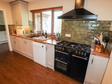 A kitchen with wooden countertops black stove and oven white cabinets and a window with blinds at Bryn Elsi in Betws-Y-Coed