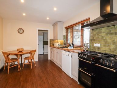 A kitchen with a wooden dining table and chairs a black stove and white cabinets at Bryn Elsi in Betws-Y-Coed