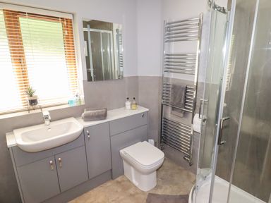 A bathroom with a sink, toilet, shower, towel rack, and window blinds at Bryn Elsi in Betws-Y-Coed