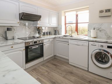 A kitchen with white cabinets a built in oven a dishwasher and washing machine at Seaview Cottage in Salthouse Norfolk
