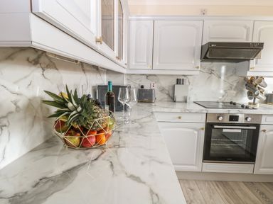 A kitchen with white cabinets marble countertops fruit bowl wine bottle and glasses at Seaview Cottage in Salthouse Norfolk
