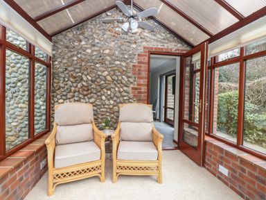 A conservatory with two armchairs a small side table and a ceiling fan at Seaview Cottage in Salthouse Norfolk