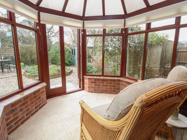 A conservatory with wicker furniture and a view of a garden at Seaview Cottage in Salthouse Norfolk