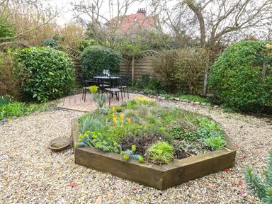 A garden with a raised flower bed surrounded by gravel and a patio with a black metal table and chairs Seaview Cottage Salthouse Norfolk