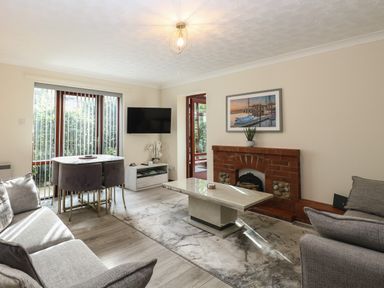 A living room with a brick fireplace a coffee table sofas a dining table with chairs and a wall-mounted television at Seaview Cottage in Salthouse Norfolk