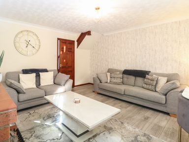 A living room with two grey sofas a white coffee table wall clock and wooden door at Seaview Cottage in Salthouse Norfolk