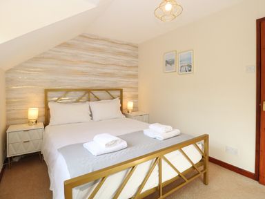 A bedroom with a gold bed frame white bedding two bedside tables with lamps and two framed pictures on the wall at Seaview Cottage in Salthouse Norfolk