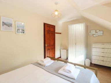 A bedroom with a bed folded towels on the bed a wooden door white wardrobe white dresser and framed pictures on the wall at Seaview Cottage in Salthouse Norfolk
