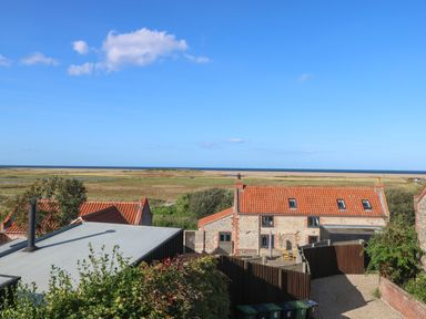 A view of stone cottages with orange roofs overlooking fields and the sea at Seaview Cottage in Salthouse Norfolk