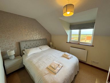 A bedroom with a double bed with white linens bedside tables with lamps and a window showing rooftops at Seaview Cottage in Salthouse Norfolk