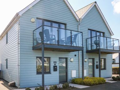 A two-story house with blue siding and glass balconies with chairs at Seaquel in Westward Ho