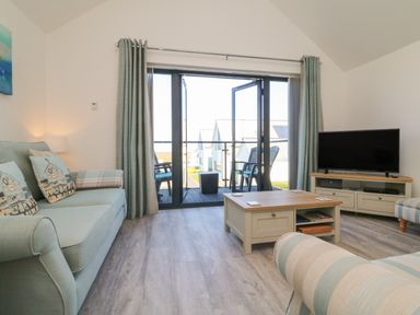 A living room with sofas a coffee table a tv and glass doors leading to a balcony at Seaquel in Westward Ho